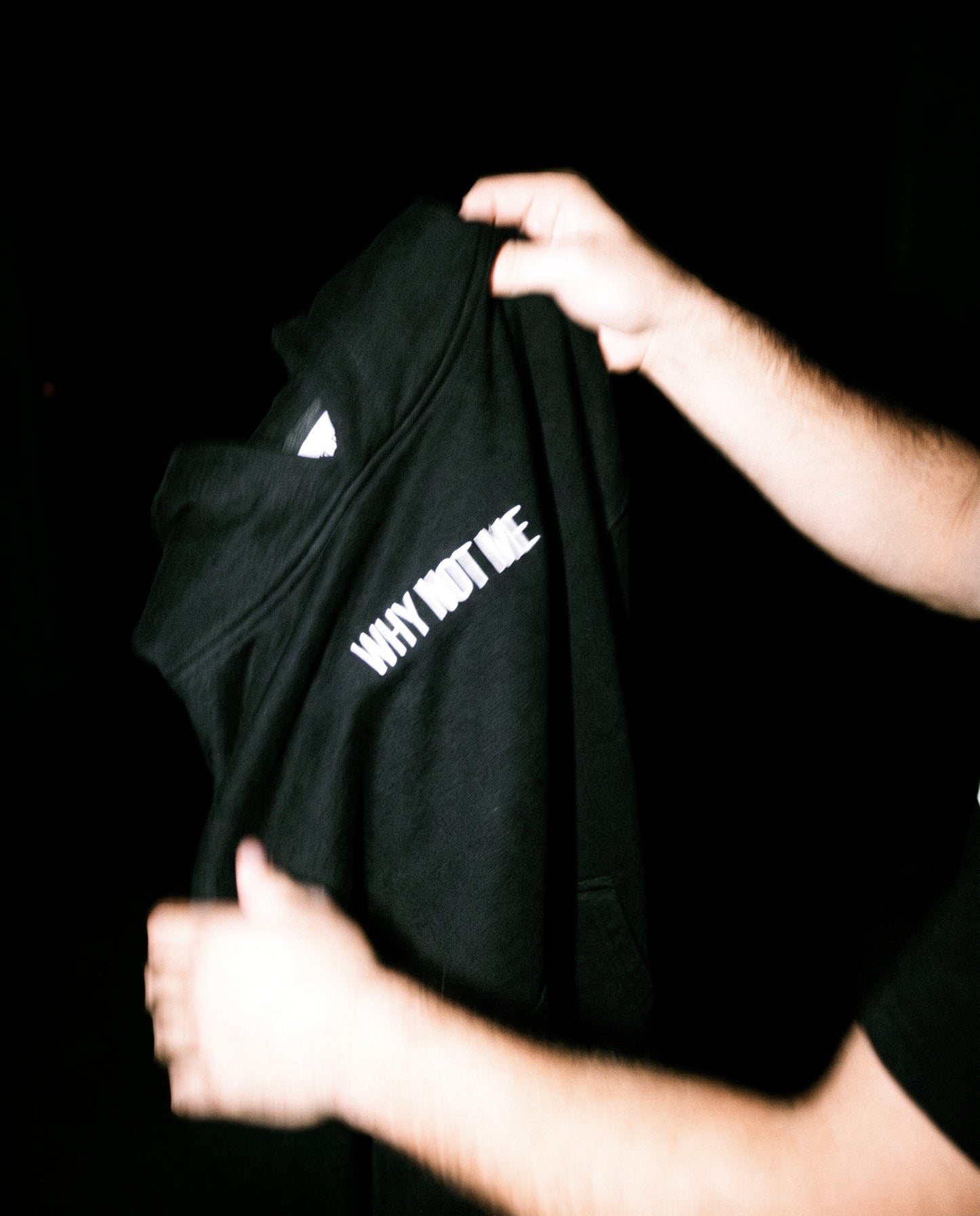 THE RESET hoodie held in hands, embroidered WHY NOT ME in white on black fleece